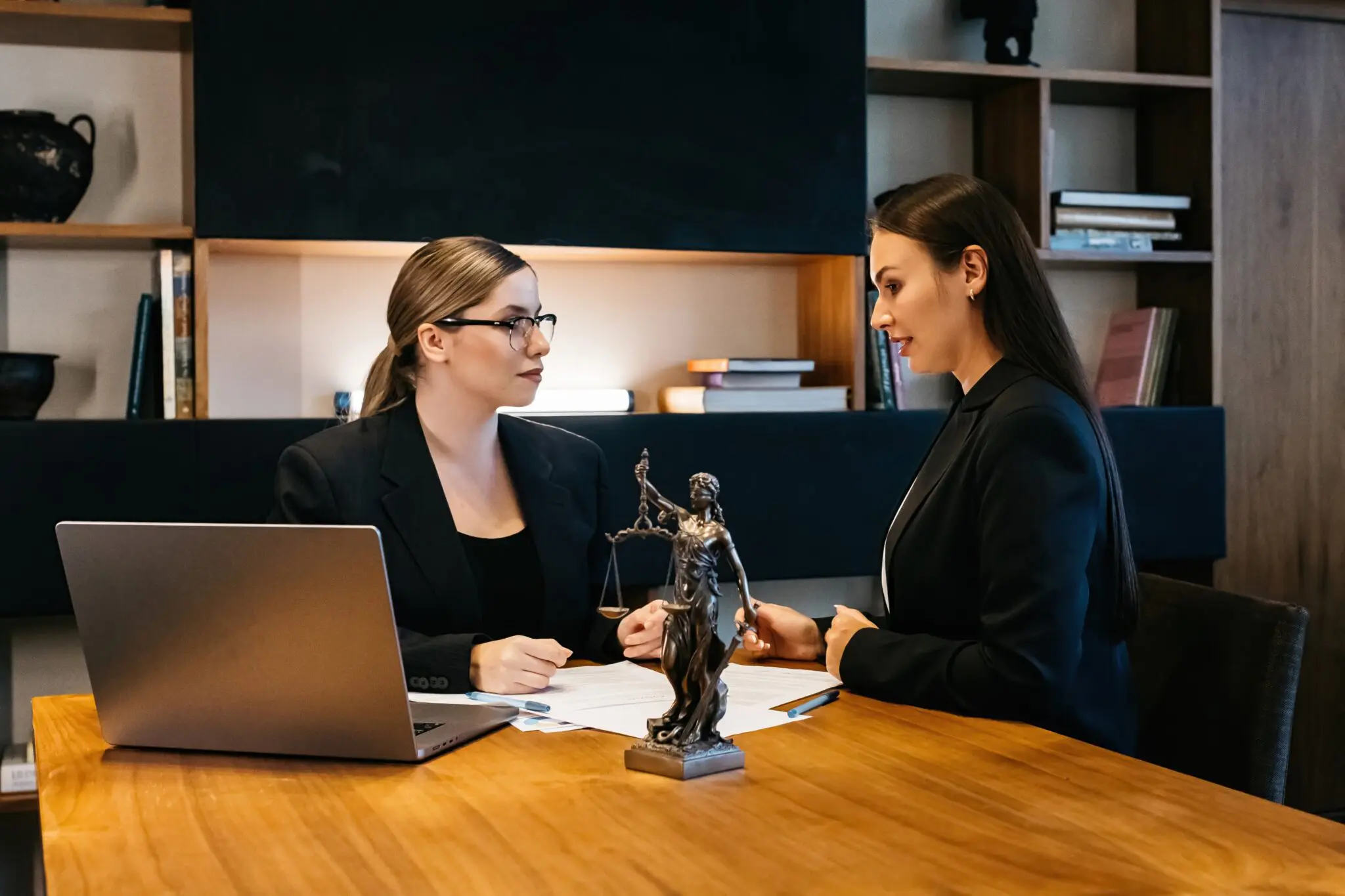 Two women discussing at a wooden table.